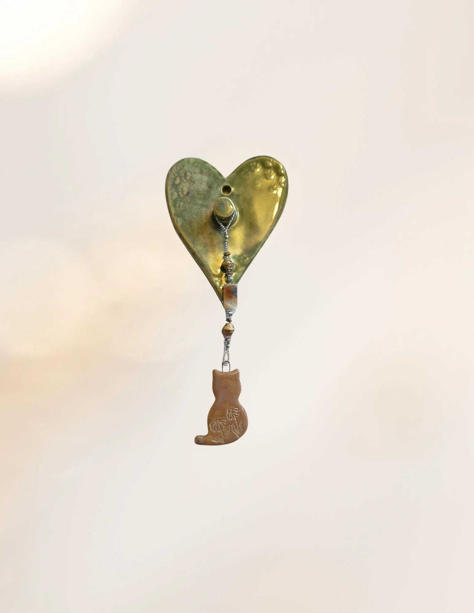 A metallic wind chime in the shape of a heart with a boot at the bottom, hanging from a string.