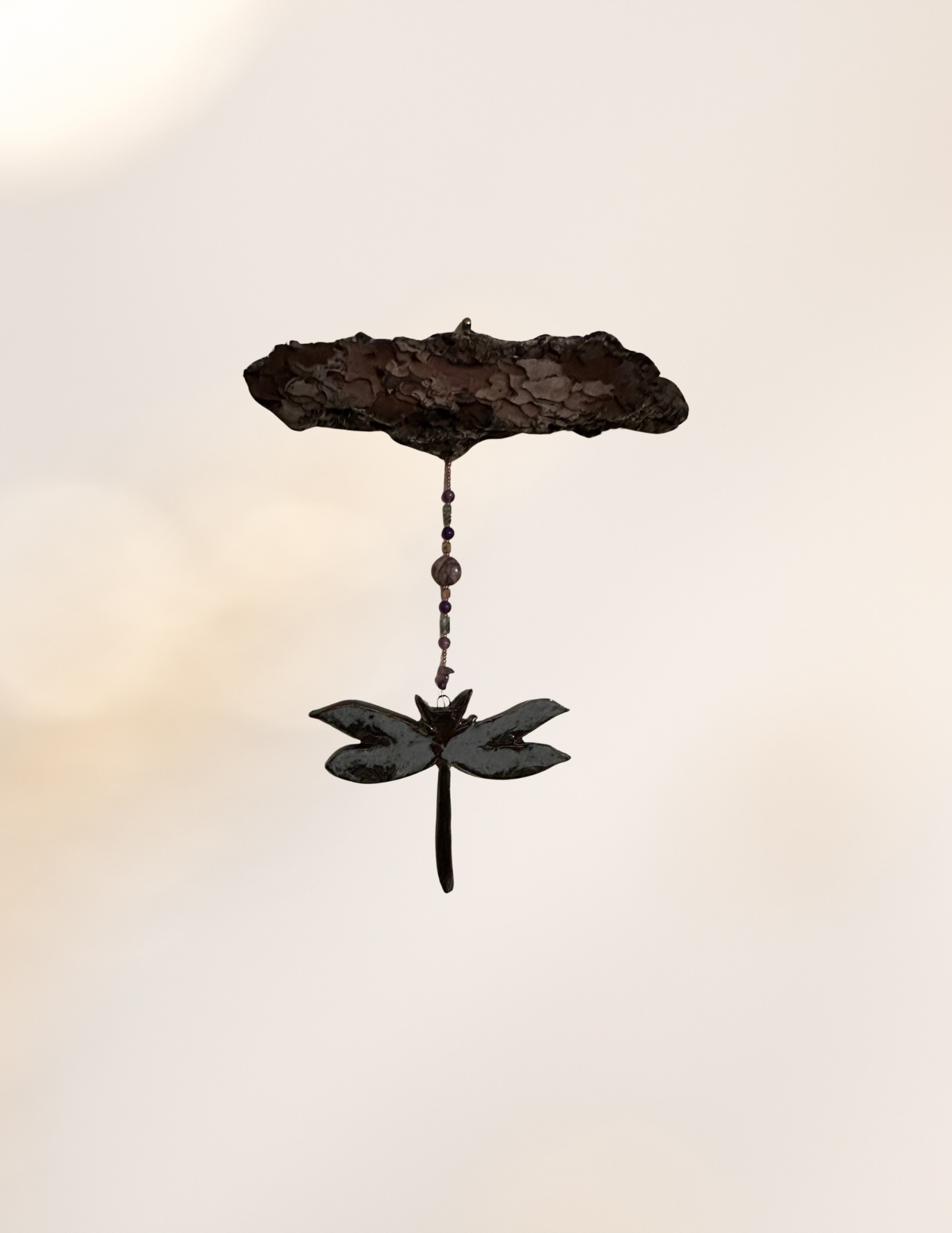 A decorative metal hanging ornament with a large flower, a butterfly, and a circular element, suspended from a string with beads.