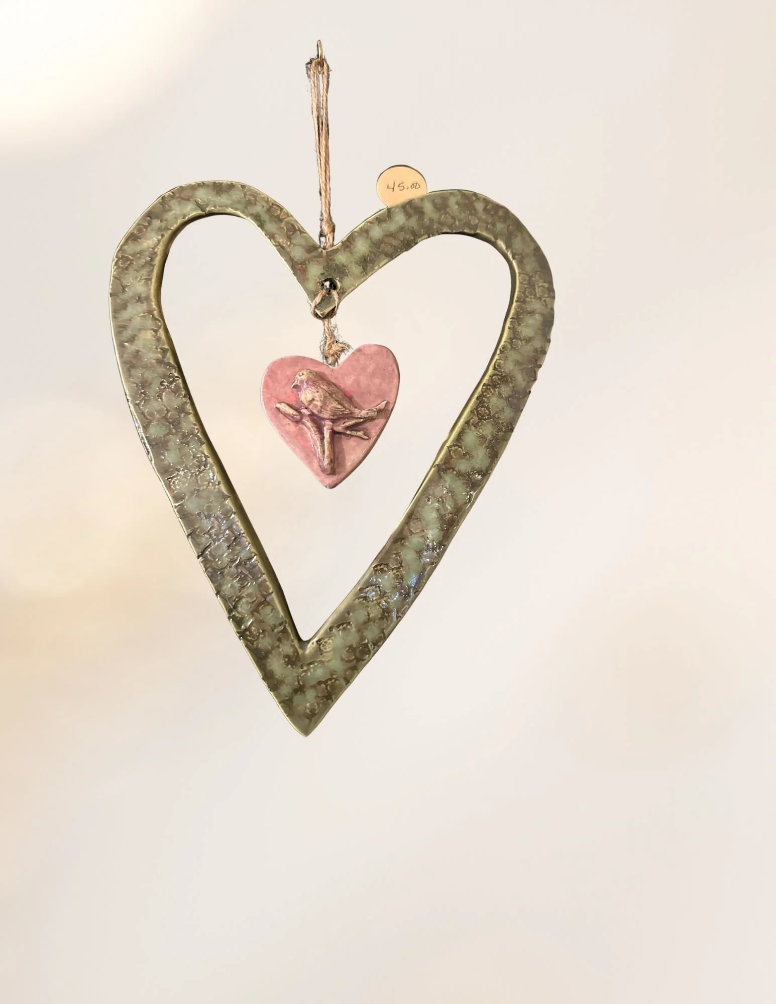 Decorative heart-shaped metal frame with a pink heart and bird ornament inside, hanging by a string with a price tag of 45 dollars.