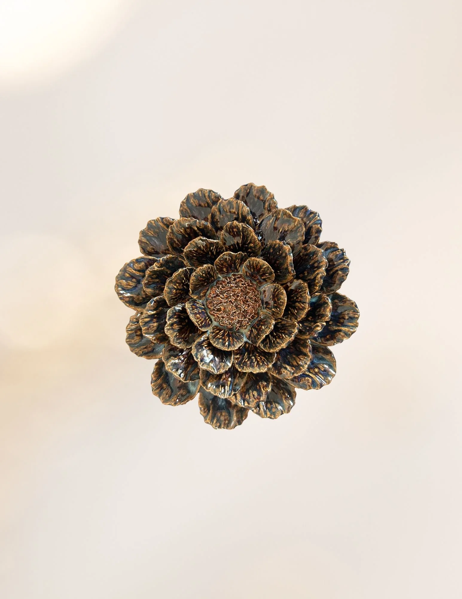 A metallic pine cone sculpture with detailed, layered scales reflecting light, placed on a plain white background.