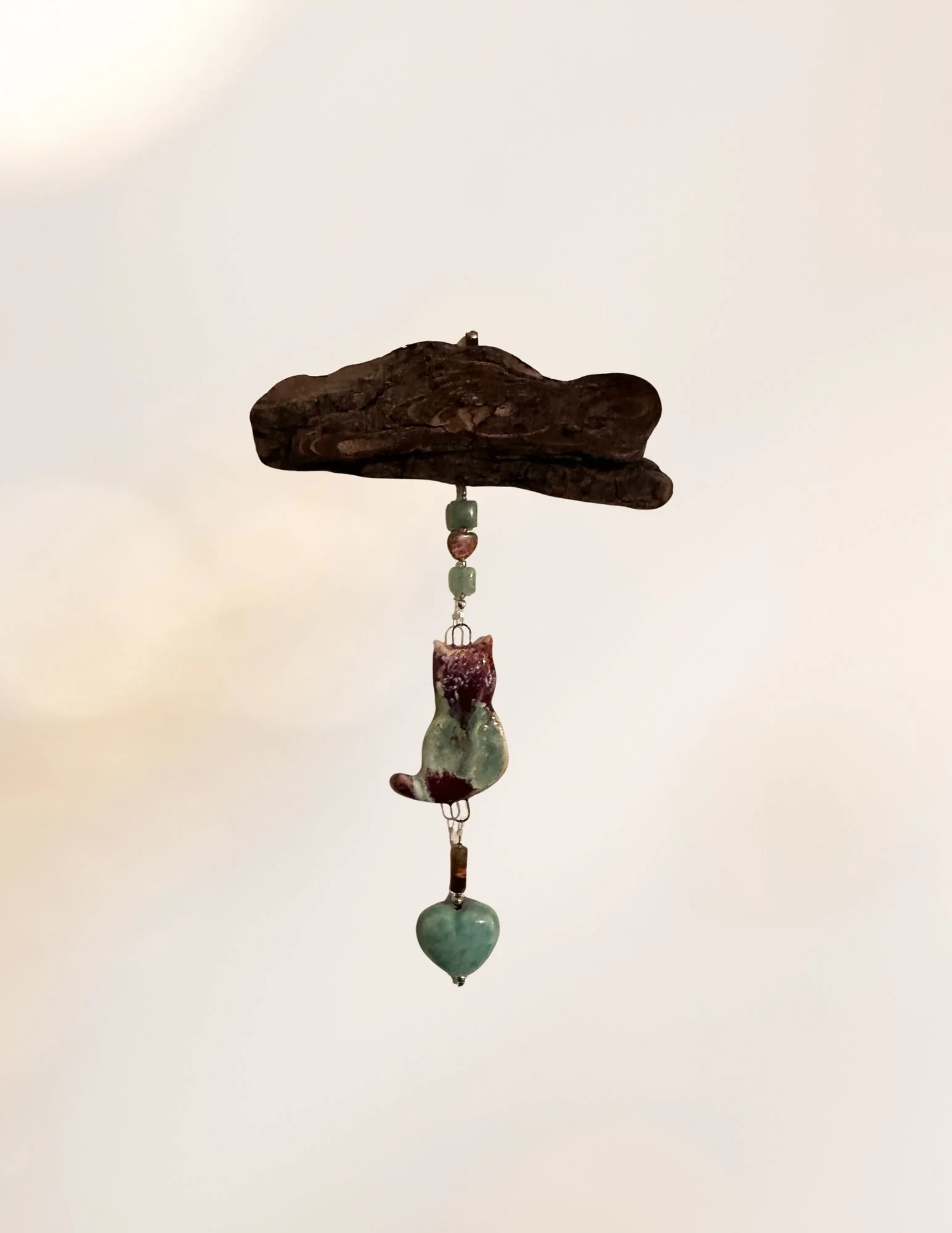 A wind chime with a piece of driftwood at the top, hanging colorful beads and jade stones against a plain background.