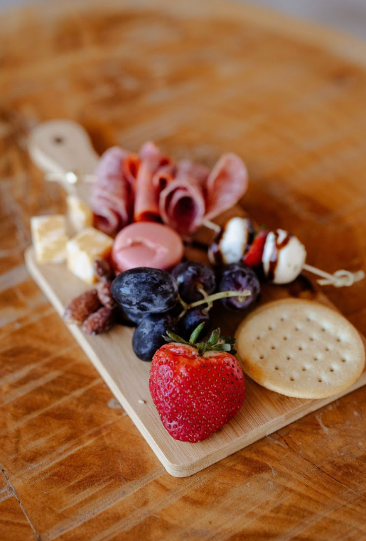 Cheese, grapes, strawberries, cookies, and various meats on a wooden serving board.