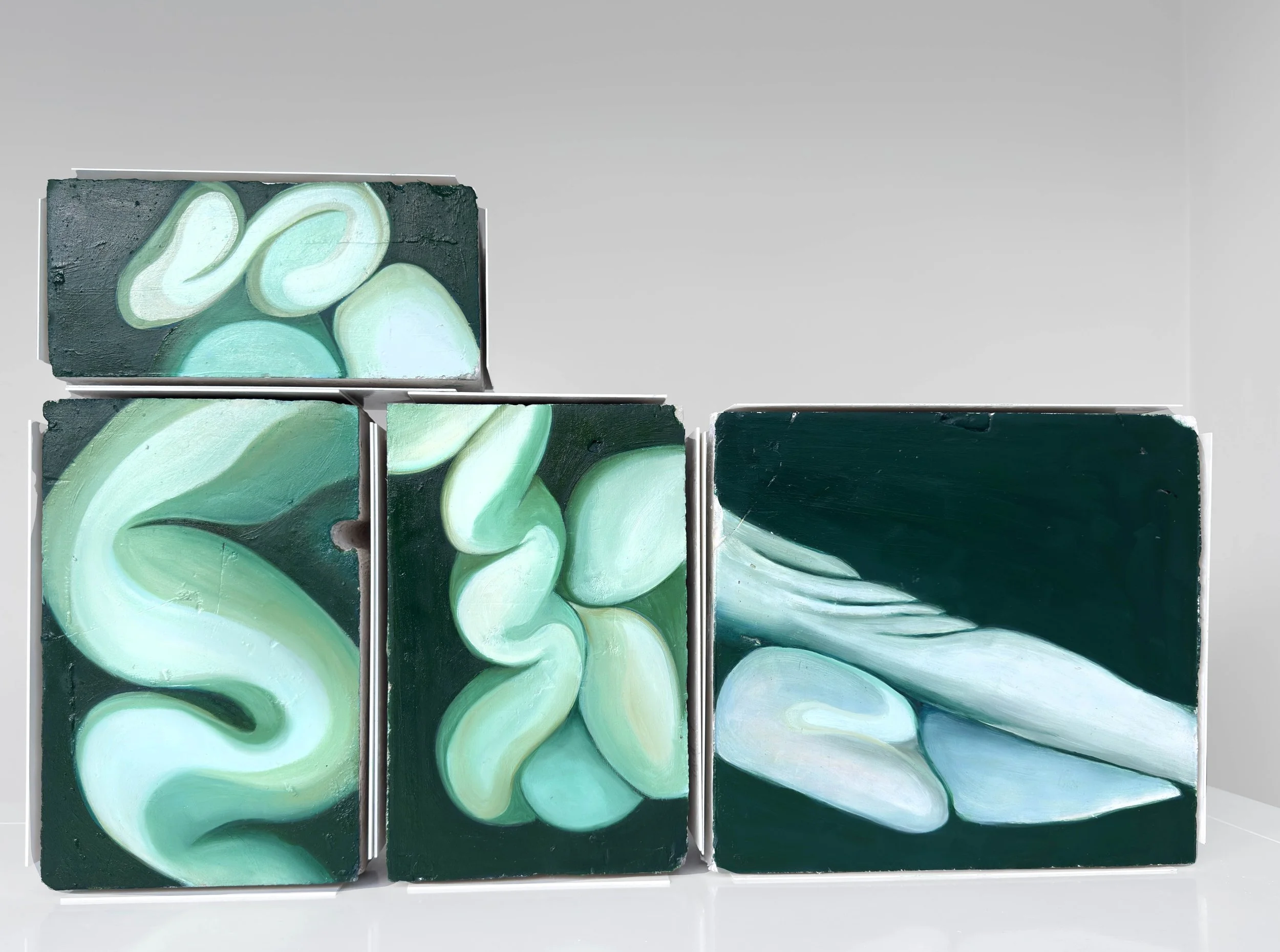 Cuadros abstractos en tonos verdes y azulados, exhibidos en un marco metálico, en una pared gris clara.
