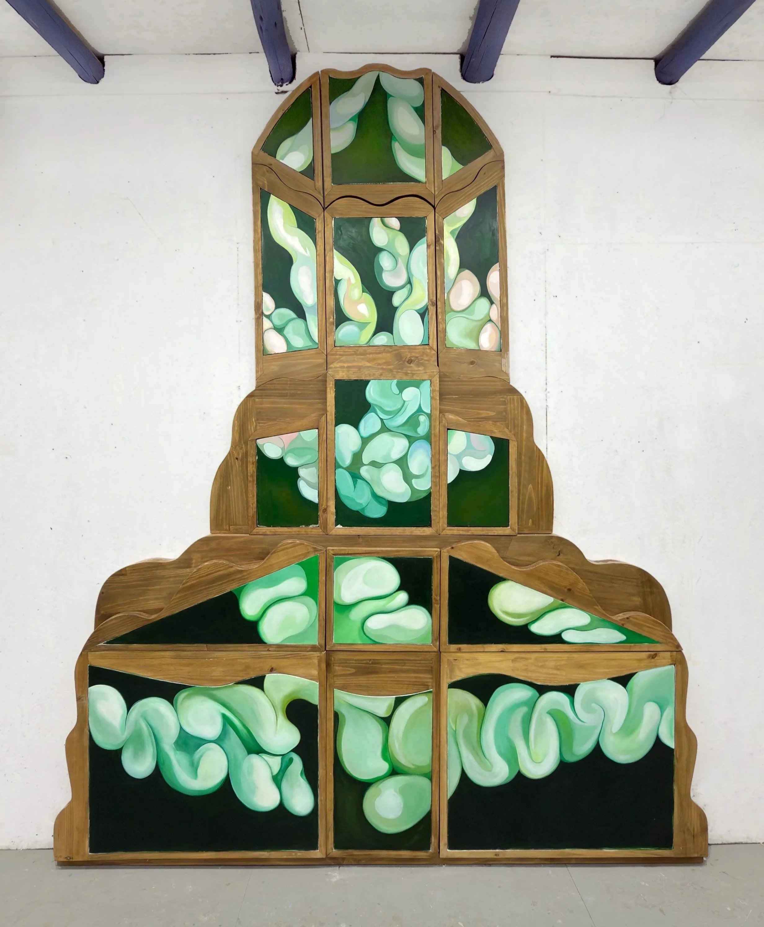 Estructura de madera decorada con paneles pintados con formas y tonos de verdes y blancos, parece un árbol o estructura artística