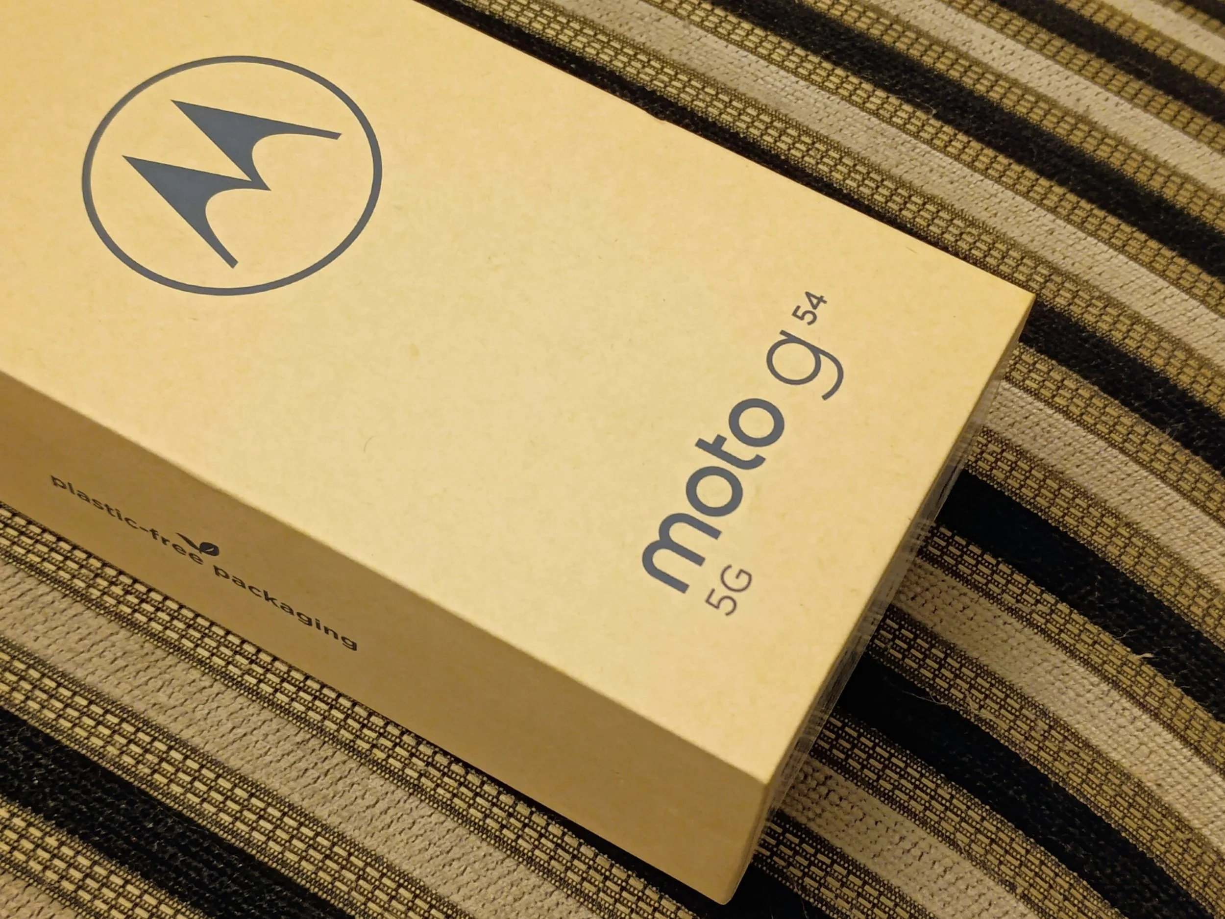 Yellow packaging box with a black and yellow striped border on a textured surface, showing a logo with a lightning bolt and text indicating it is a plastic-free packaging for a 55G product.