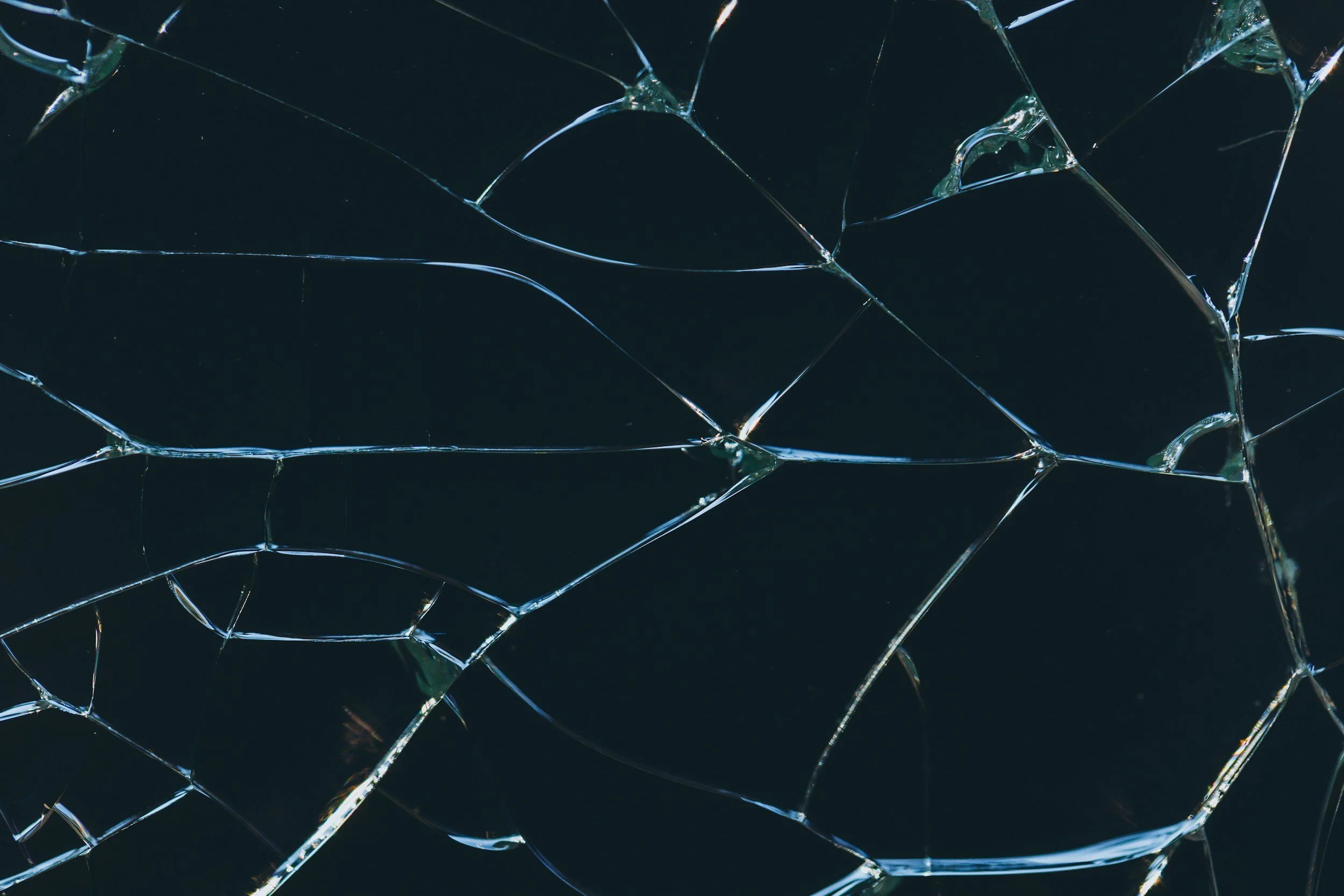 Close-up of a shattered glass surface with sharp, irregular cracks and jagged edges, dark background.