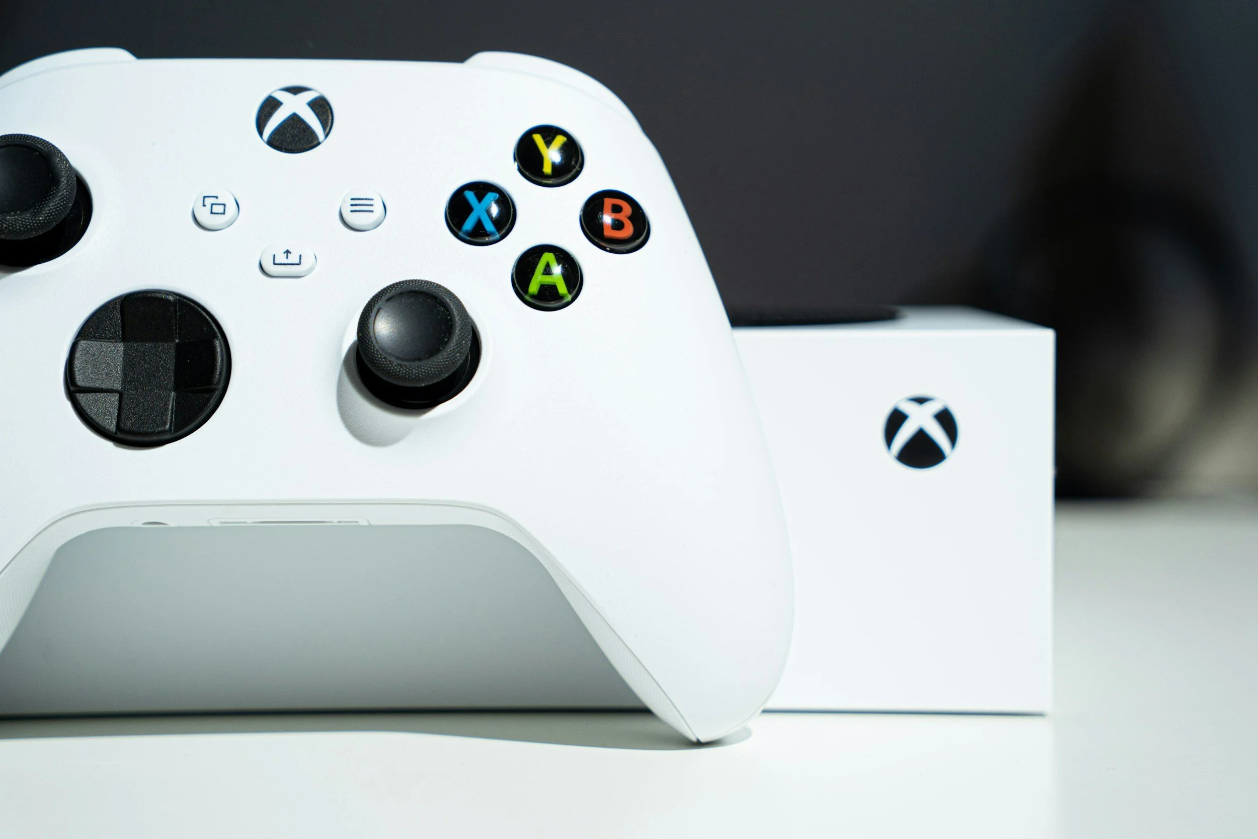 Close-up of a white Xbox Series X/S controller with colorful buttons, resting on its white box against a black background.