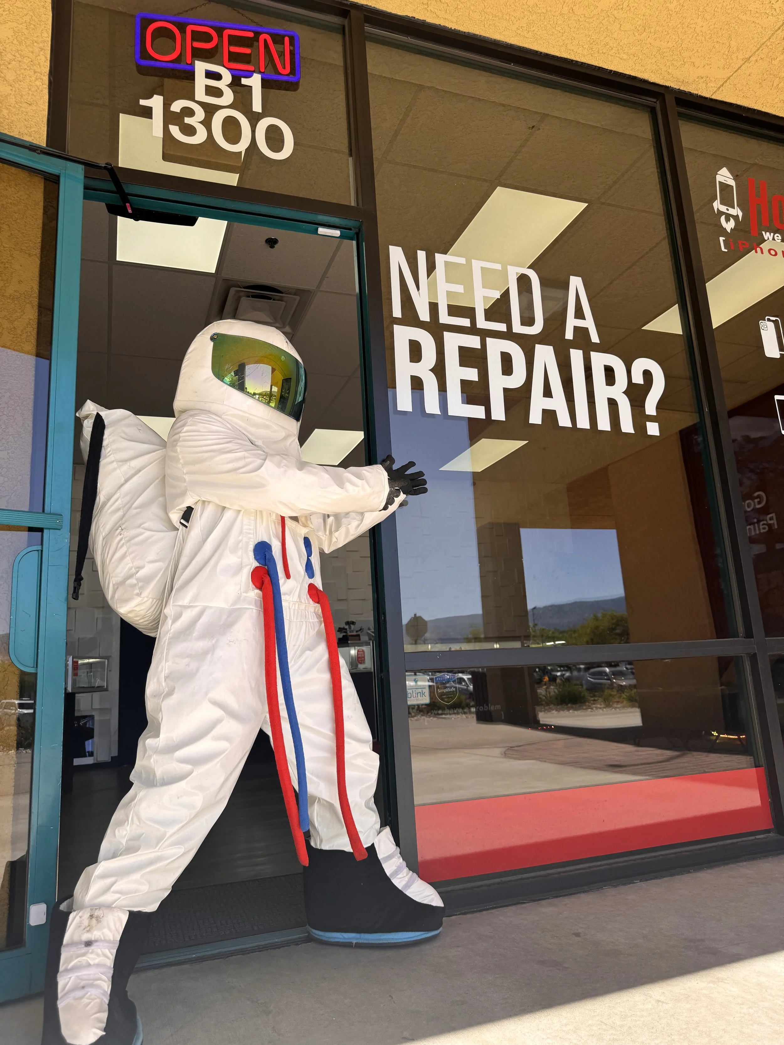 A figure wearing a spacesuit, kneeling inside a glass entrance door to a store with an 'Open' neon sign, and the words 'Need a Repair?' on the window.