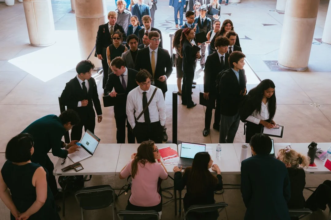 Group of young people waiting in line inside a building, likely participating in a registration or check-in process at an event or conference.