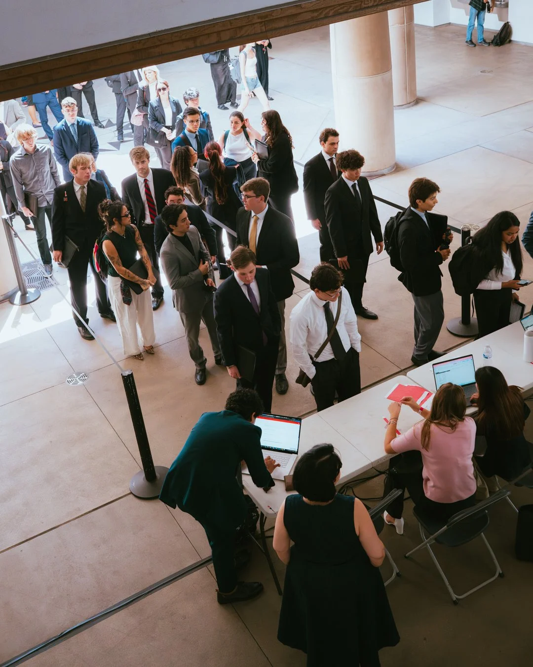 A group of diverse young professionals in business attire standing in line at a check-in desk in a modern building.