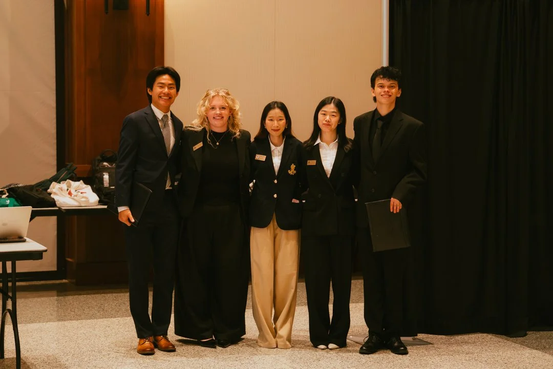 Group of five people in formal attire standing together in a conference or event setting.