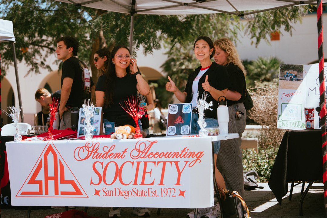 Students at a booth for the Student Accounting Society at San Diego State University, established in 1972, with decorations and informational displays at an outdoor event.