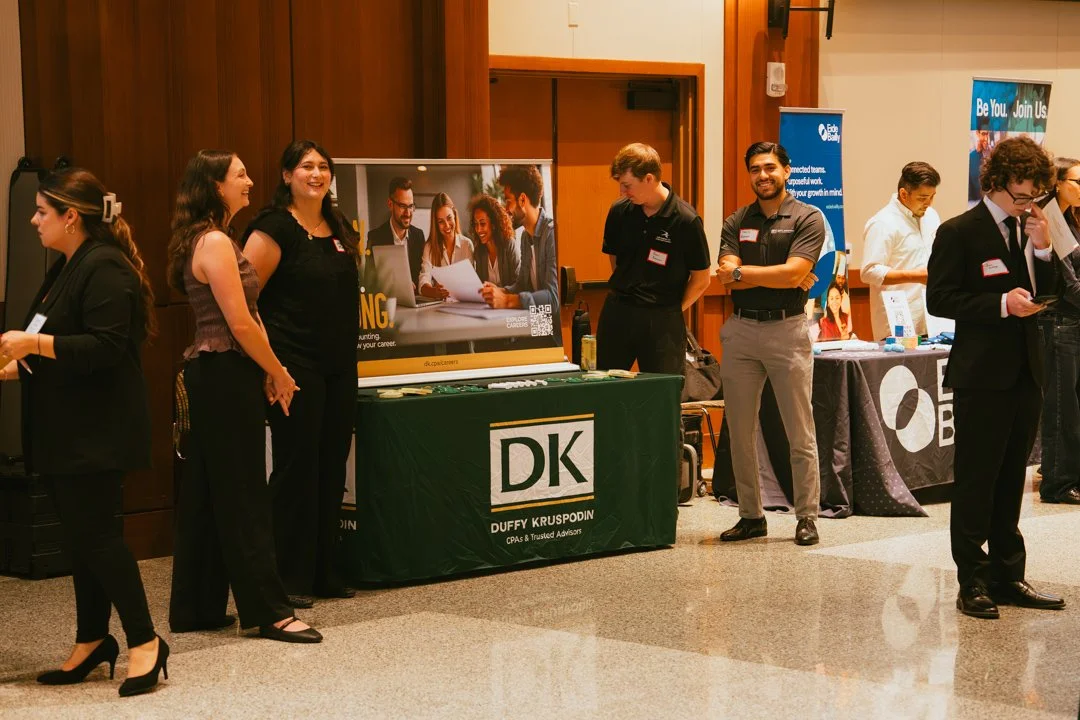 Group of people standing at a career or job fair, with booths and banners in the background.