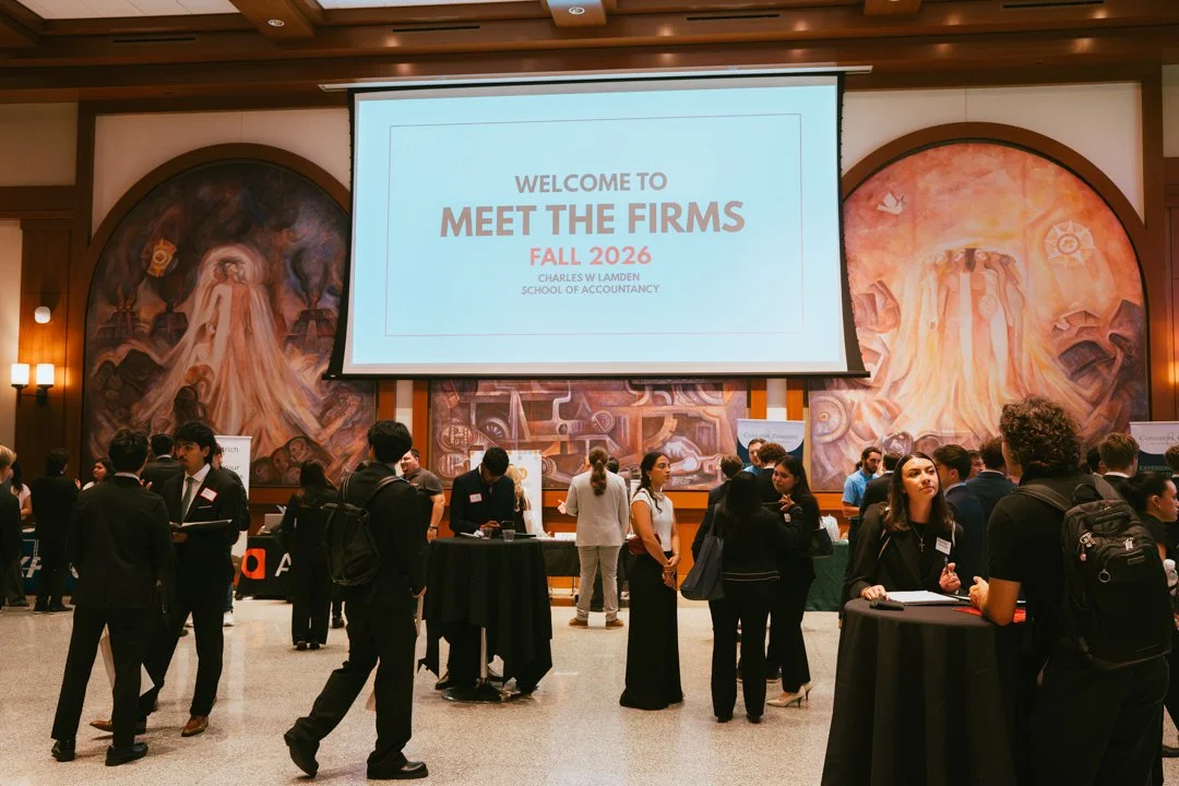 College career fair with attendees networking and booths, large screen displays 'Welcome to Meet the Firms Fall 2026 Charles L. Wlamden School of Accountancy'.