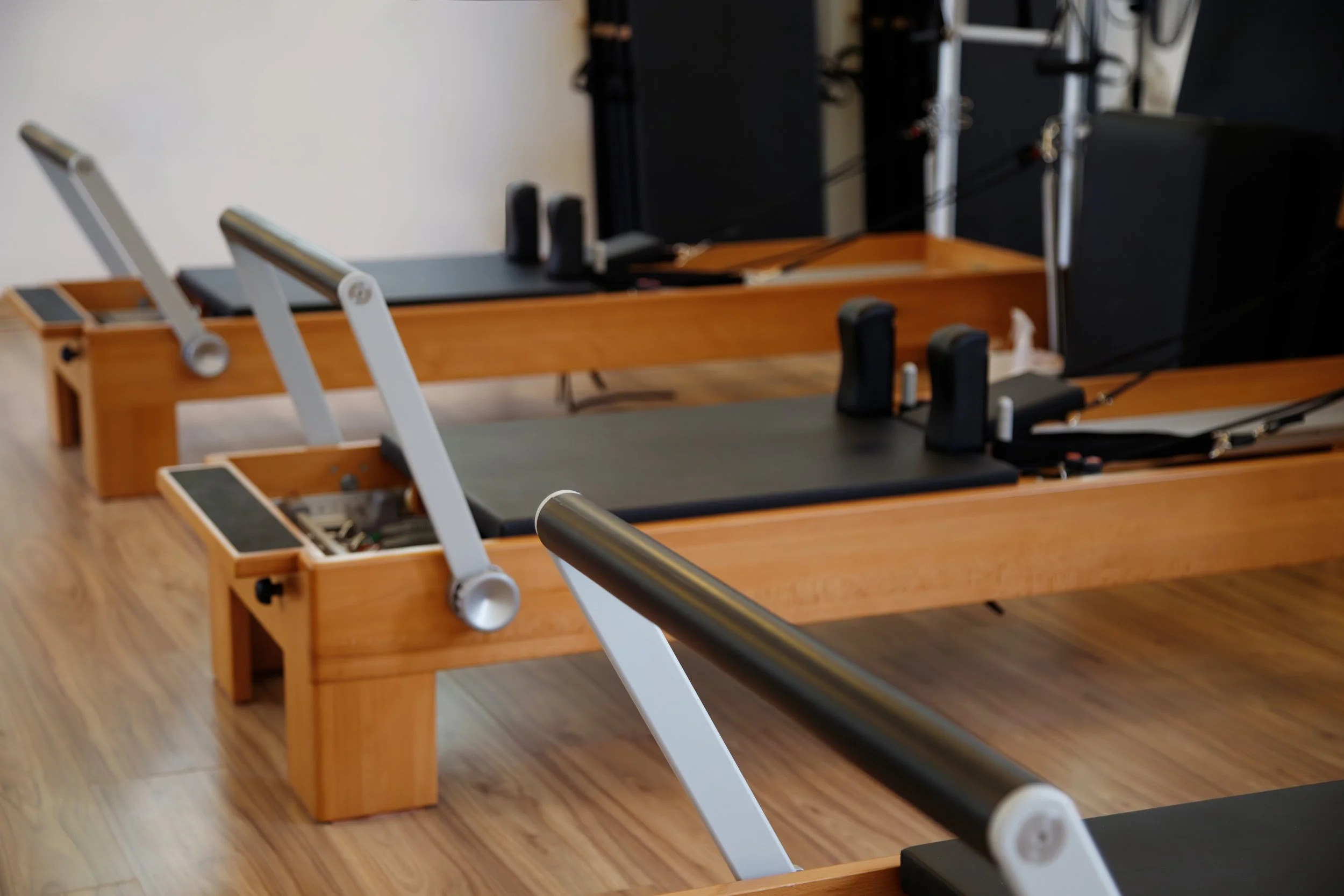 Pilates reformer machines lined up in a fitness studio with wooden floors.