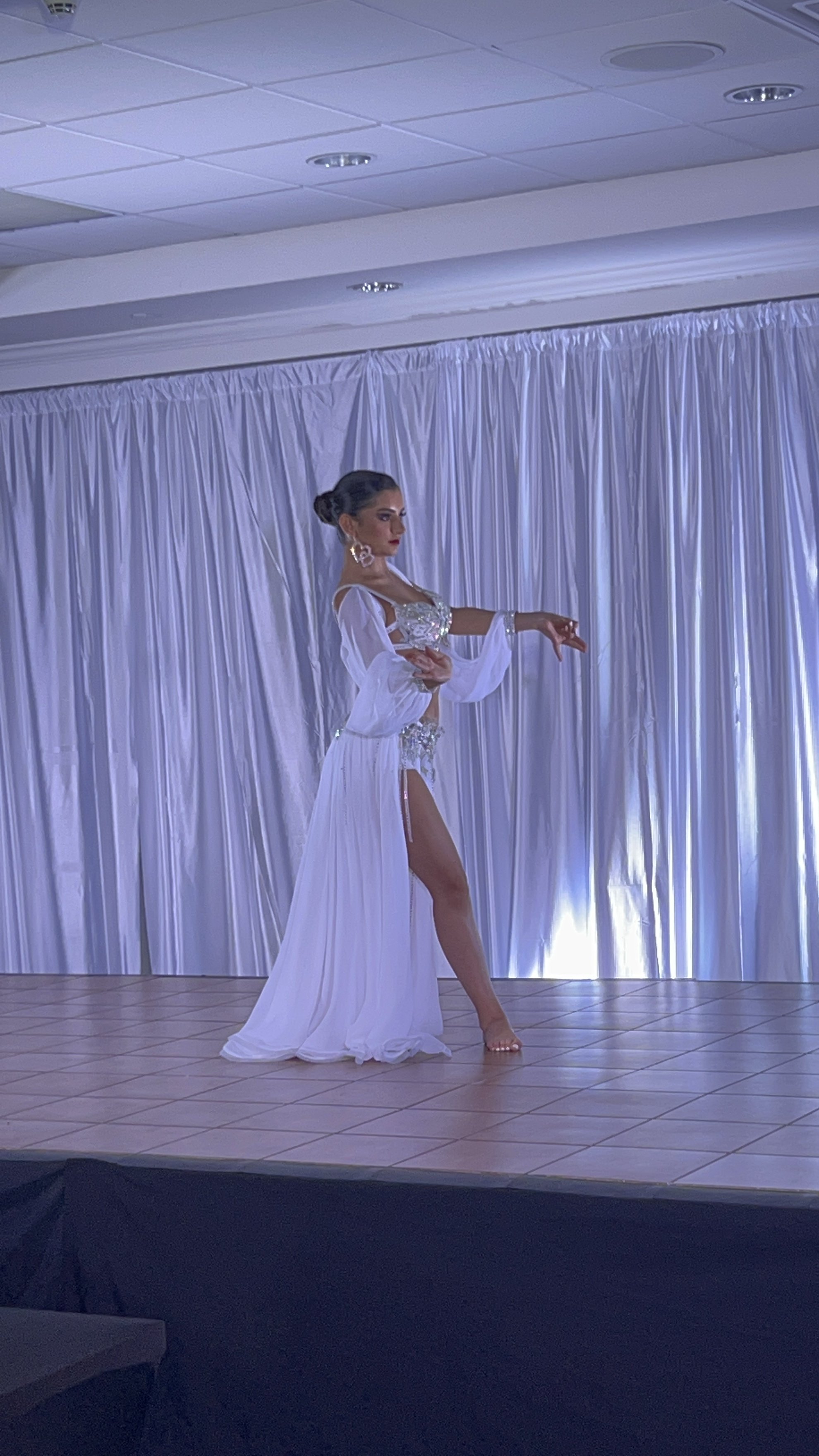 Isabella Damiani performing an Oriental dance solo in a white costume during a live stage performance.