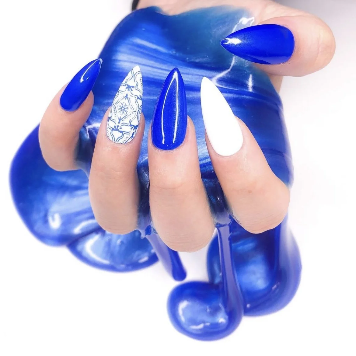 Close-up of a hand with long, pointed blue and white nails holding a blue and white marbled glass object.