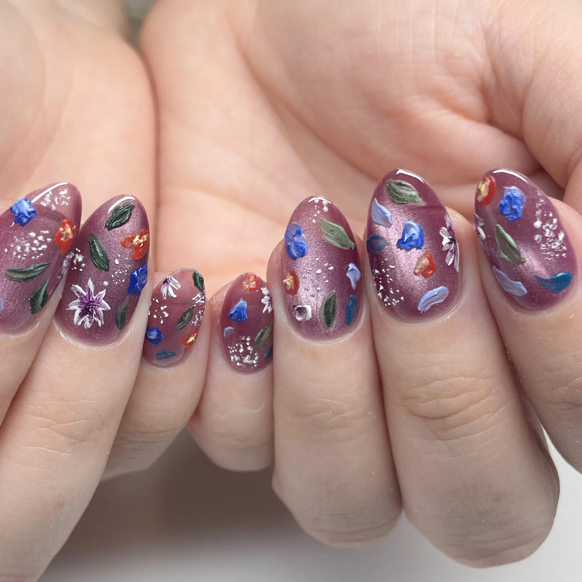 Close-up of fingernails painted with purple polish decorated with colorful floral designs