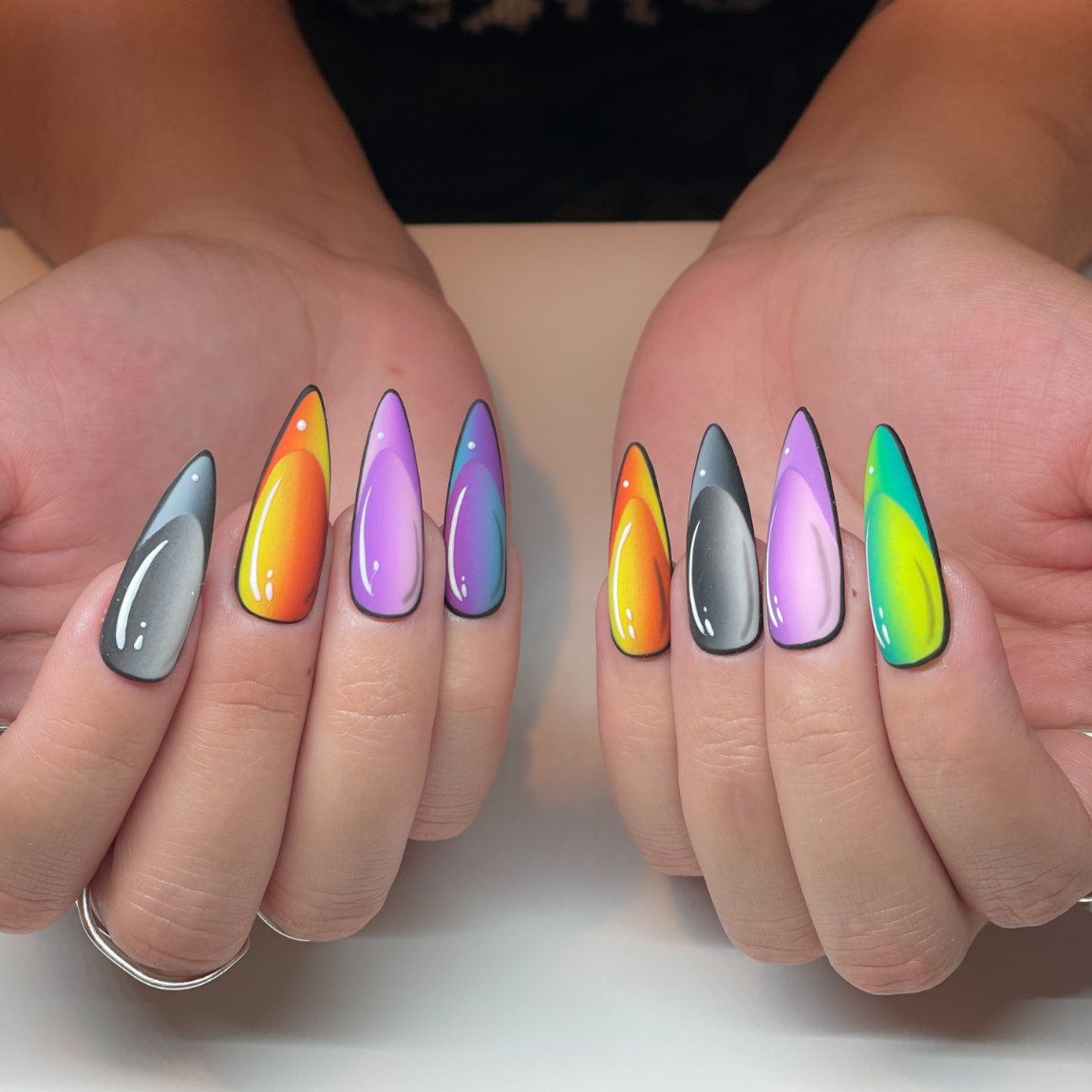 Colorful artistic nail art with a rainbow gradient and black outlines on long, almond-shaped nails.