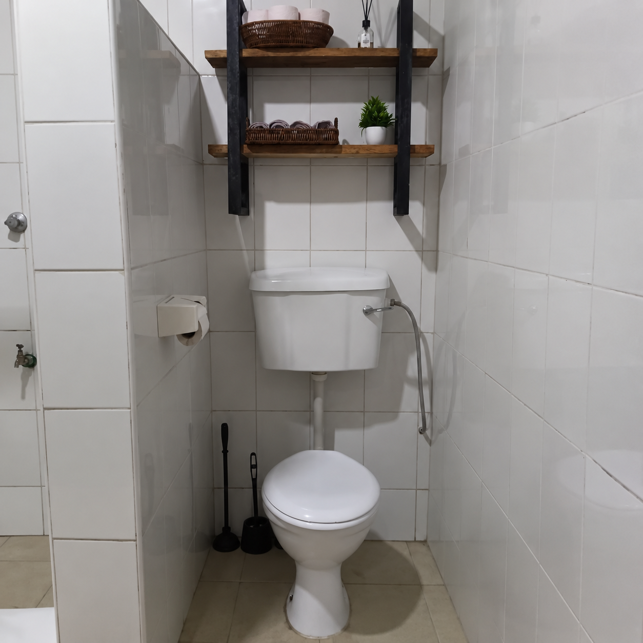 Bathroom with a white toilet, wall-mounted shelves holding baskets and decorative items, and cleaning tools stored on the floor.