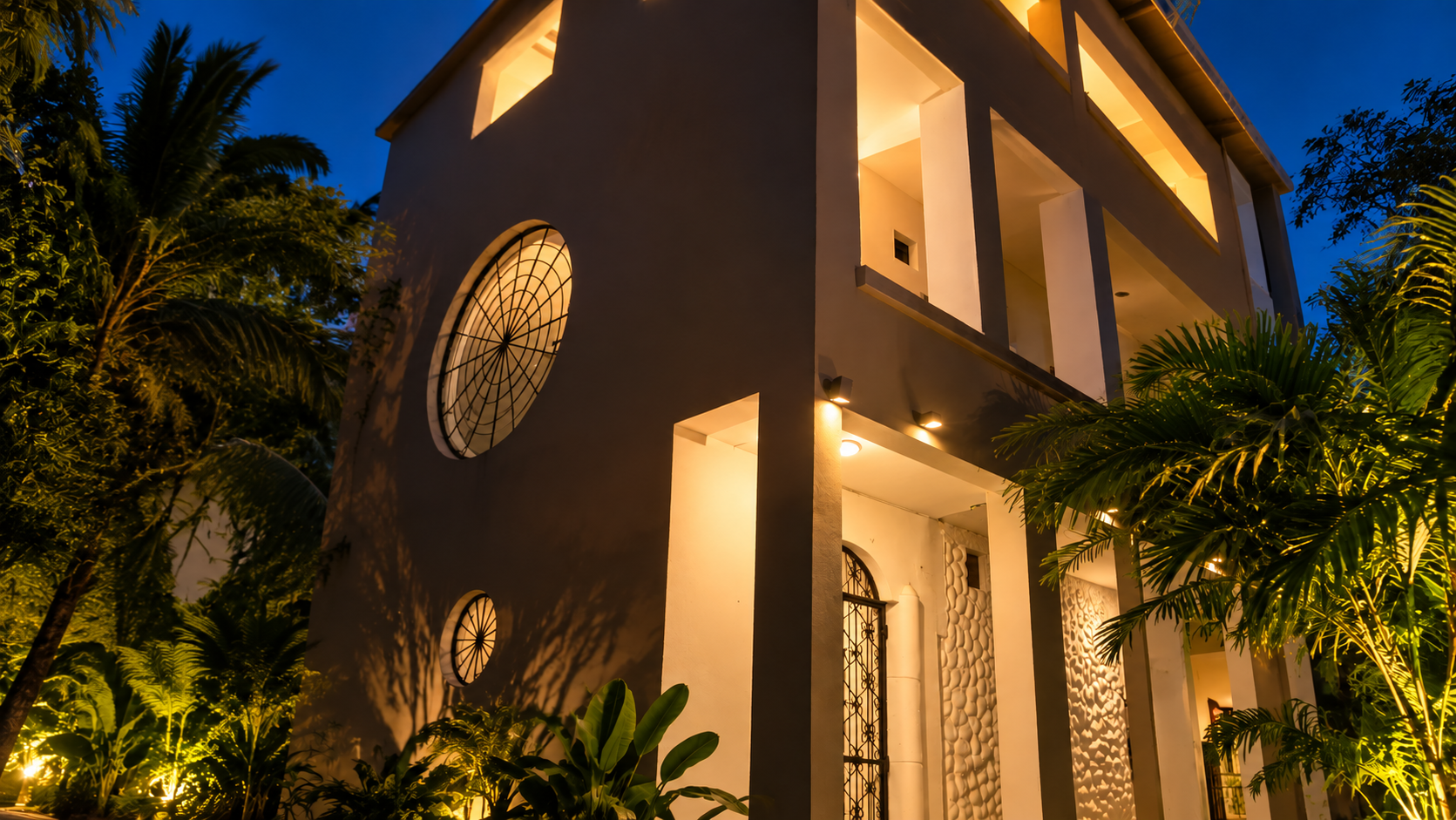 The Suites apartment exterior at night in Diani Beach, Kenya, surrounded by tropical plants.