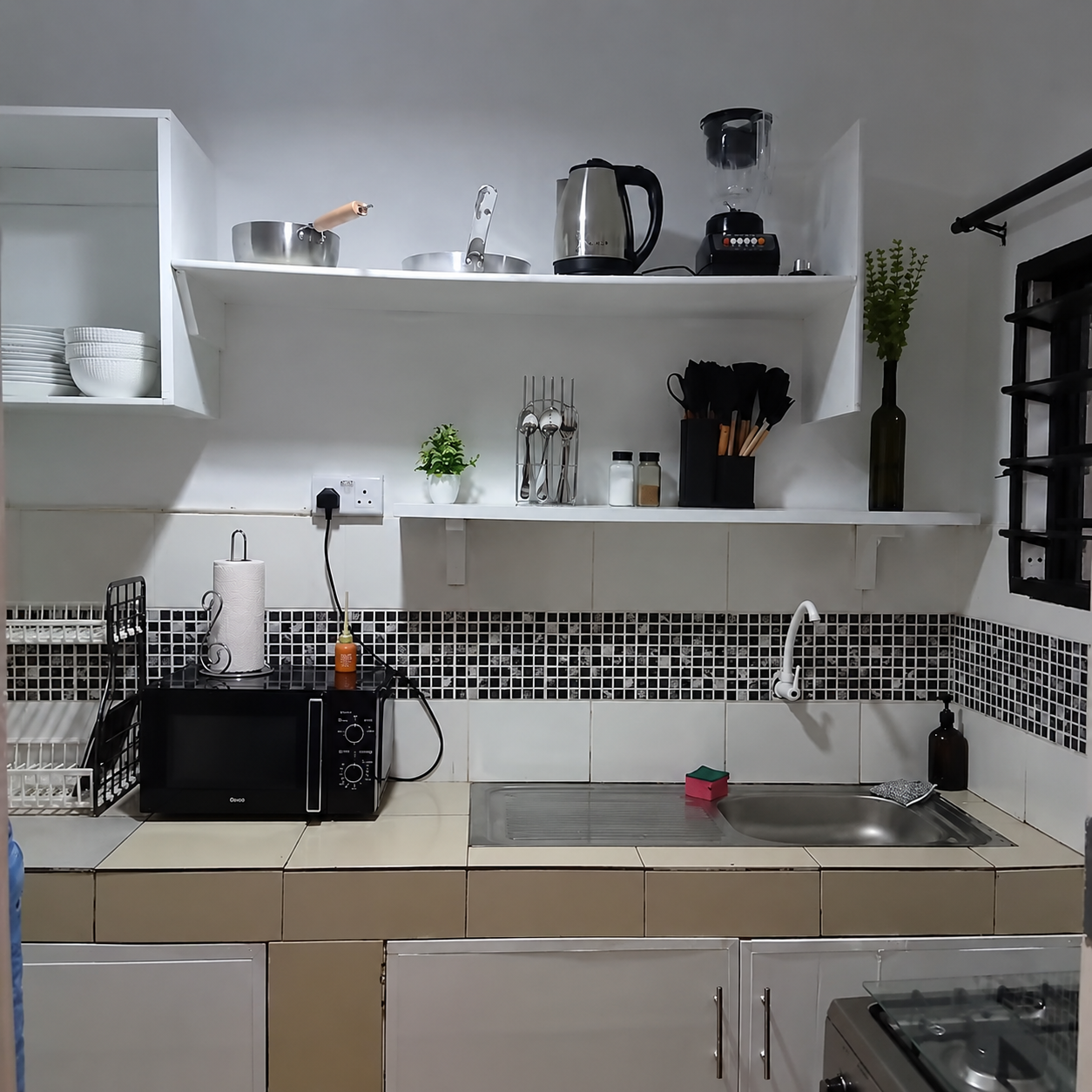 Small kitchen with white cabinets, a tiled backsplash, a sink, black microwave, and shelves with dishes and kitchen utensils.