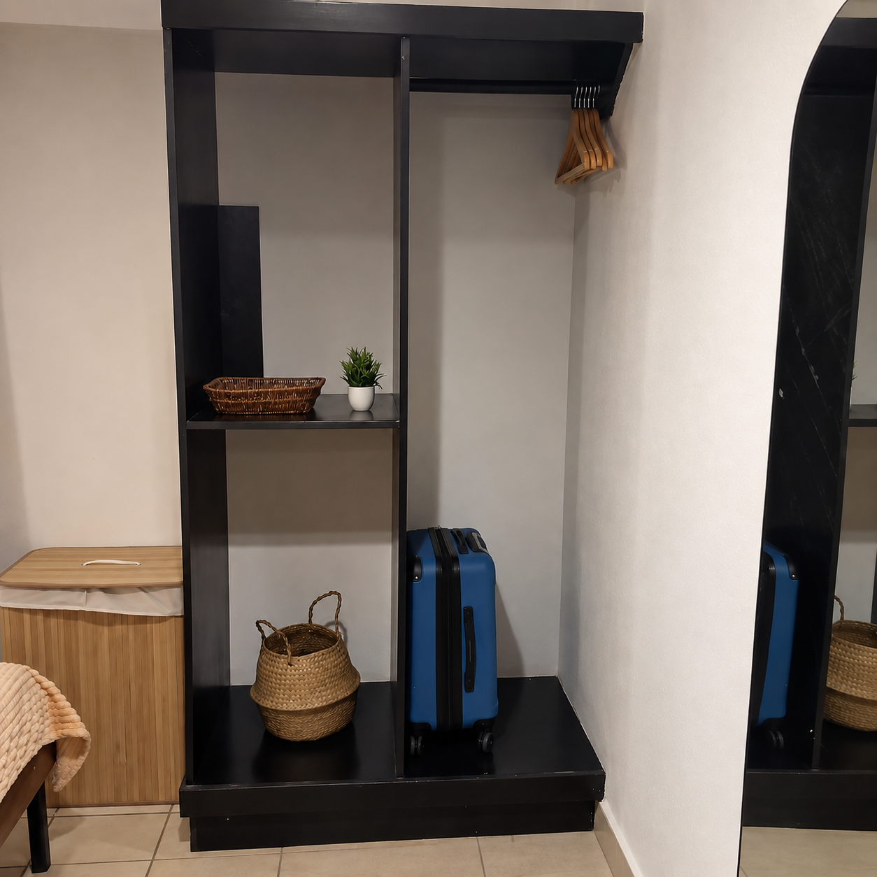 Empty black shelving unit with a few decorative items, a blue suitcase, and hanging wooden clothes hangers. A small potted plant, a wicker basket, and a woven basket are also present.