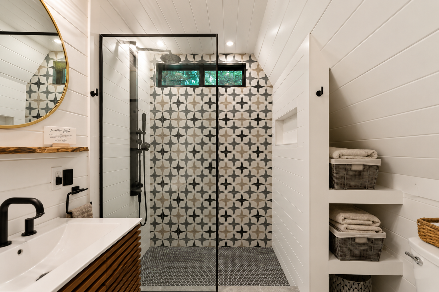 Modern bathroom with walk-in shower featuring patterned tile, white shiplap walls, and built-in shelves with towels.
