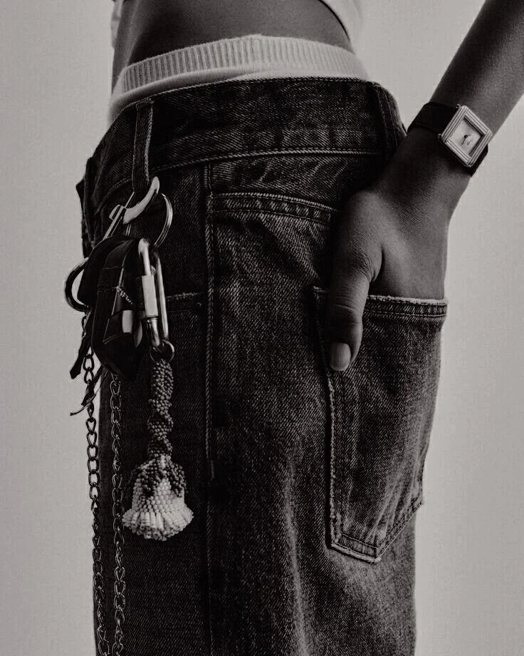 Close-up of a person wearing distressed black jeans with their right hand in the pocket, a wristwatch, and keys attached to a chain on the waist.