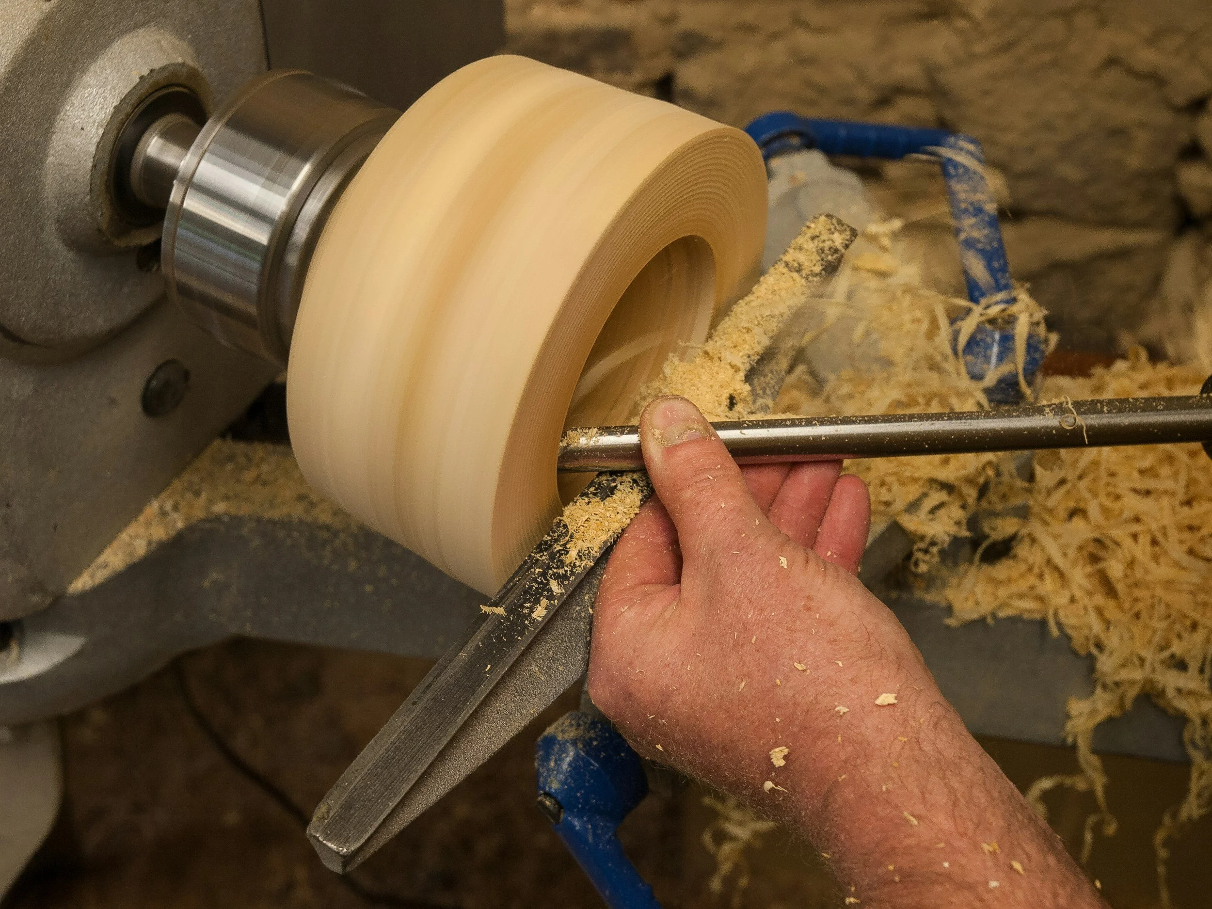 A person is turning a wooden bowl on a lathe, with wood shavings scattered around.