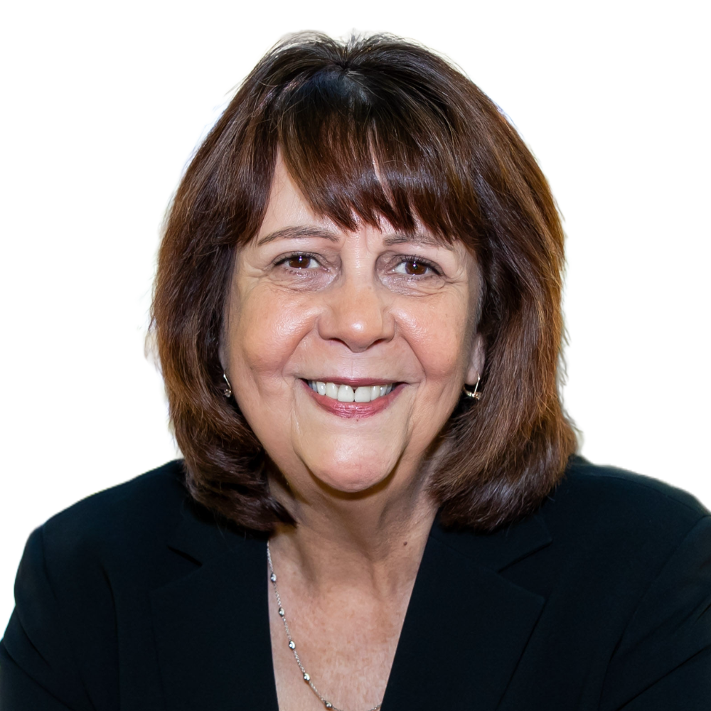A woman with shoulder-length brown hair smiling at the camera, wearing a black blazer and jewelry, against a plain white background.