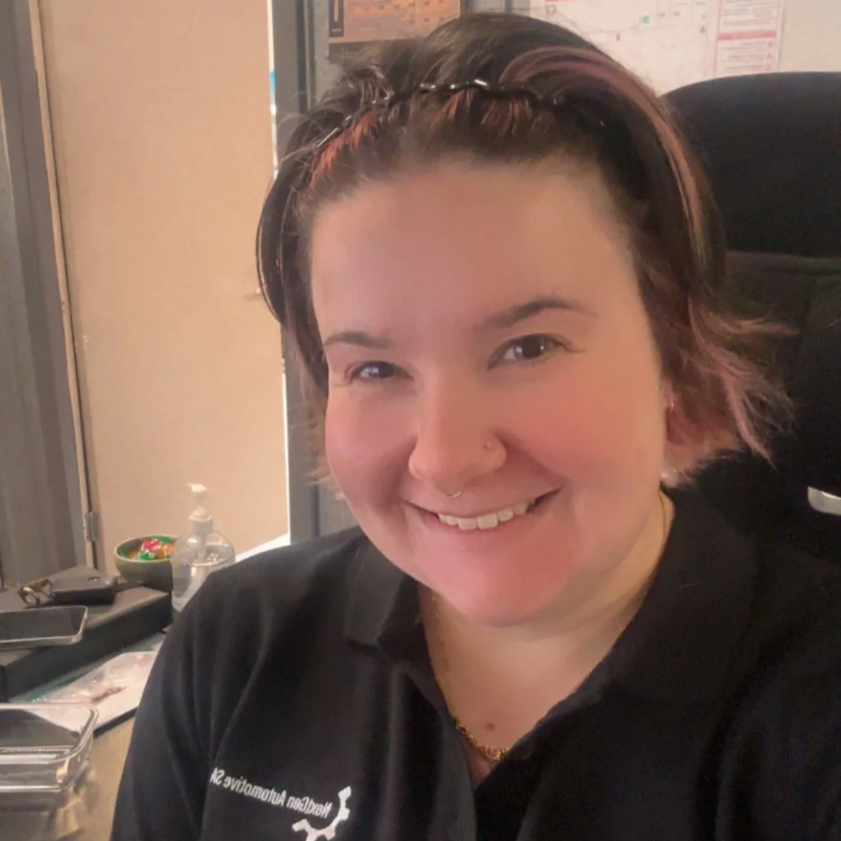 A woman with short colored hair and a nose piercing smiling at the camera in an indoor setting.