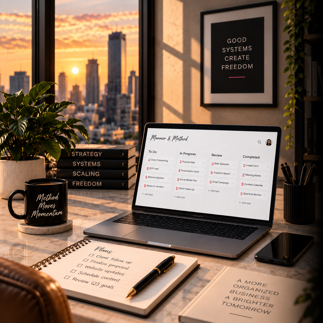 A workspace with a laptop displaying a task management app, a notebook with tasks written and checked off, a pen, a smartphone, a coffee mug with inspirational words, a plant, a stack of black books with titles like "Strategy" and "Freedom", a framed quote on the wall that says "Good systems create freedom", and a sunset city skyline seen through the window.