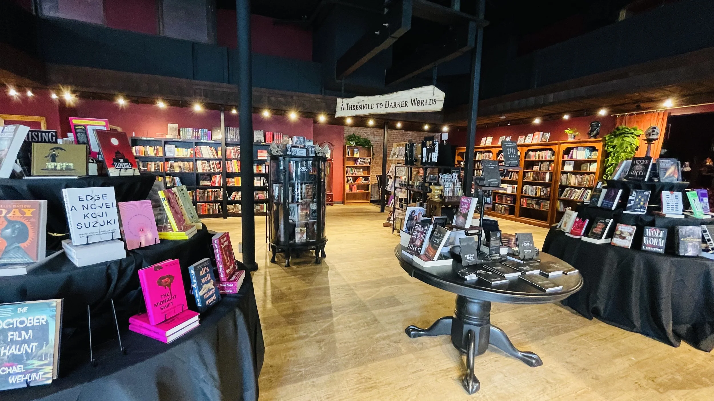Inside the horror bookstore, Infernal Annex in Olympia, Washington with multiple shelves filled with books, tables displaying new releases, and a sign that reads 'A Threshold to Darker Worlds'.