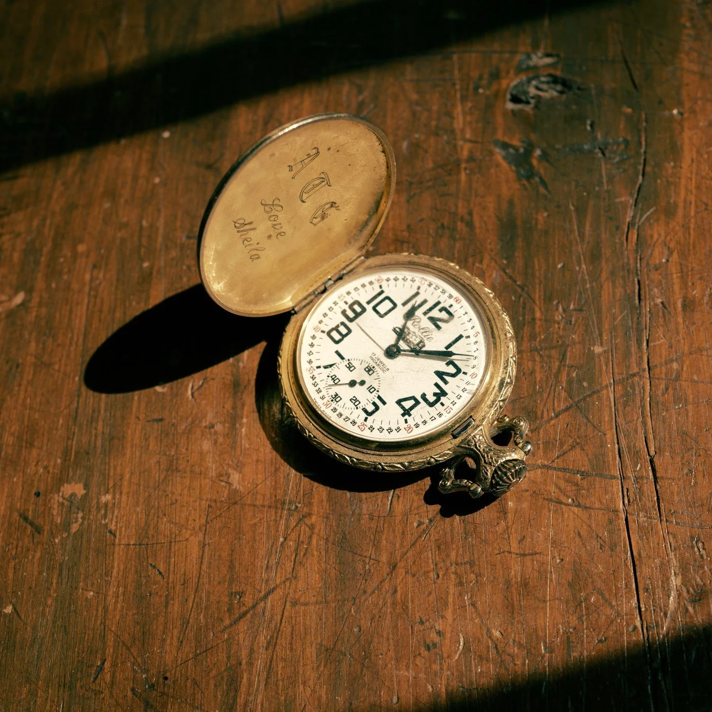Open vintage pocket watch with ornate case and engraved lid resting on a worn wooden table