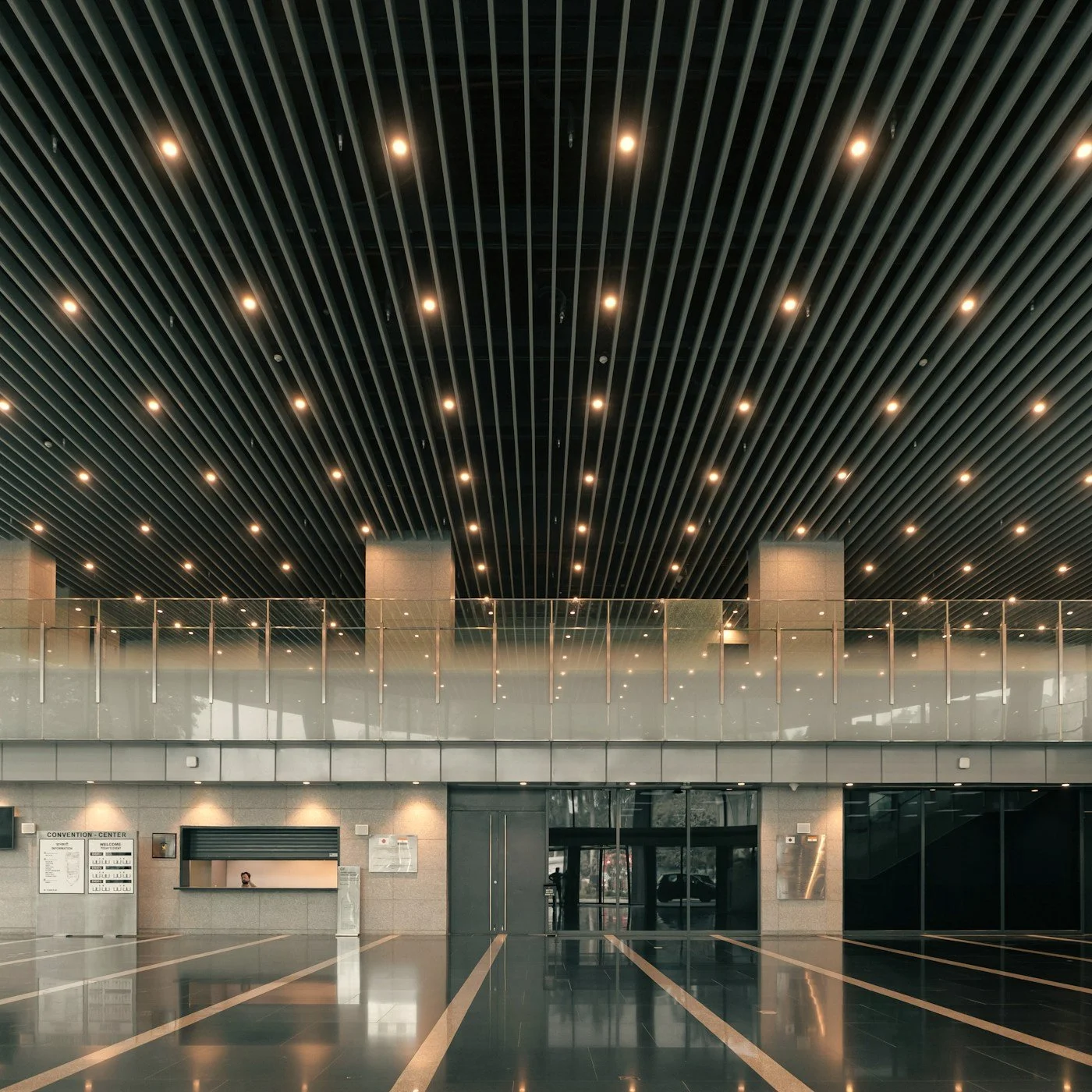 Modern convention center lobby with a ribbed ceiling, recessed lights, glass partitions, polished reflective floors, and reception desk.