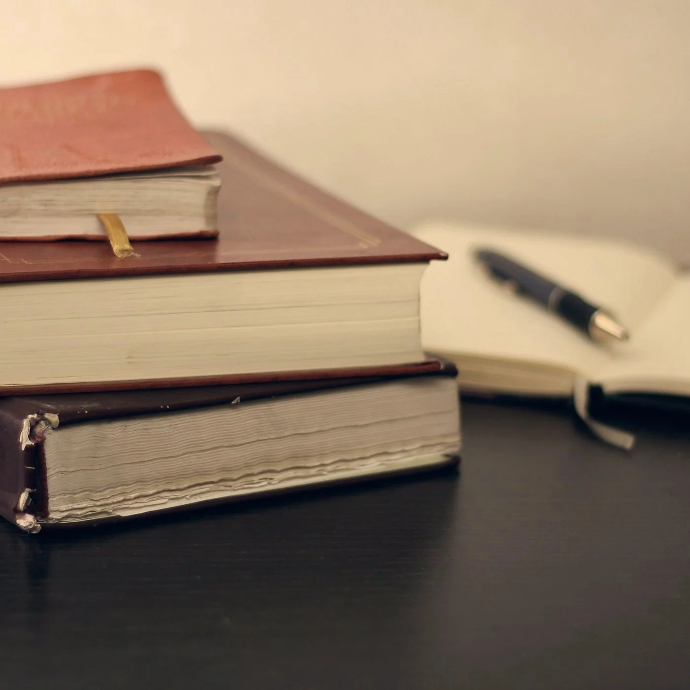 Stack of hardcover books with a leather notebook and pen on a desk