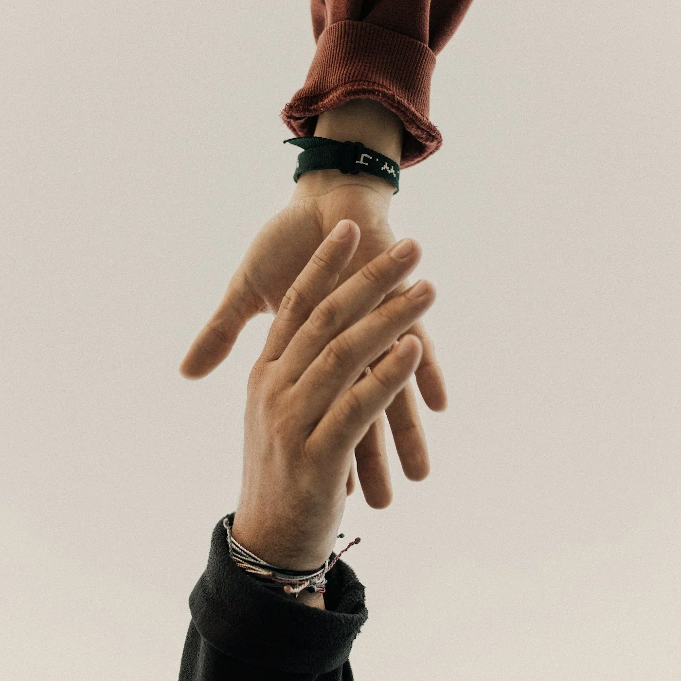 Close-up of two people reaching toward and holding each other’s hands, wearing bracelets and long sleeves.