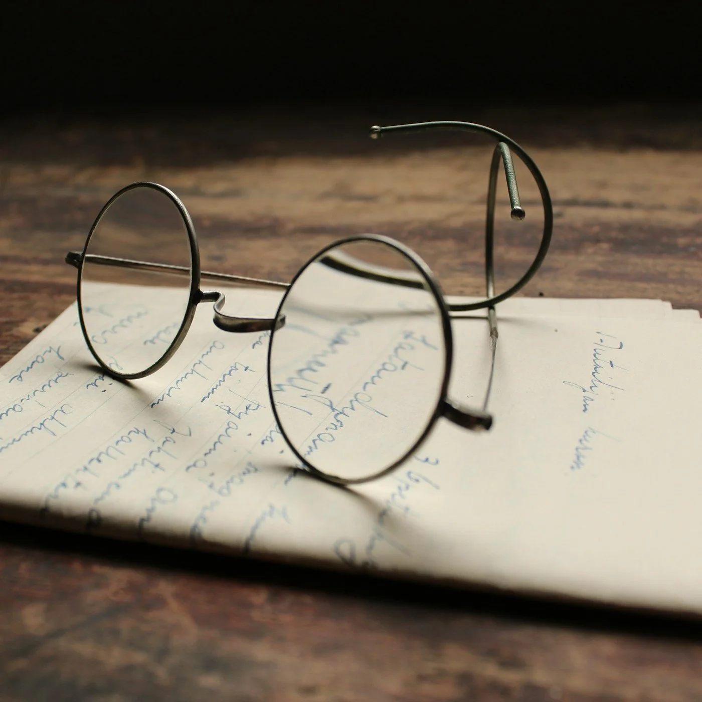 Round eyeglasses resting on handwritten notes on a wooden table