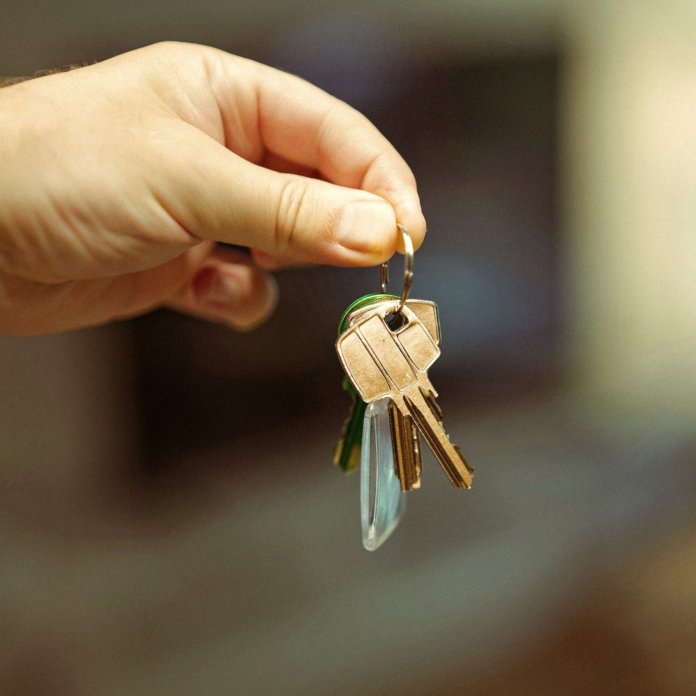 Hand holding a key ring with several house keys and a green keychain