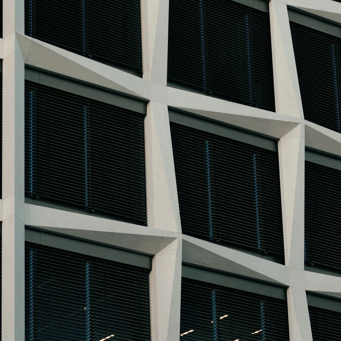 Close-up of a modern office building facade with dark horizontal window blinds and white geometric concrete framing