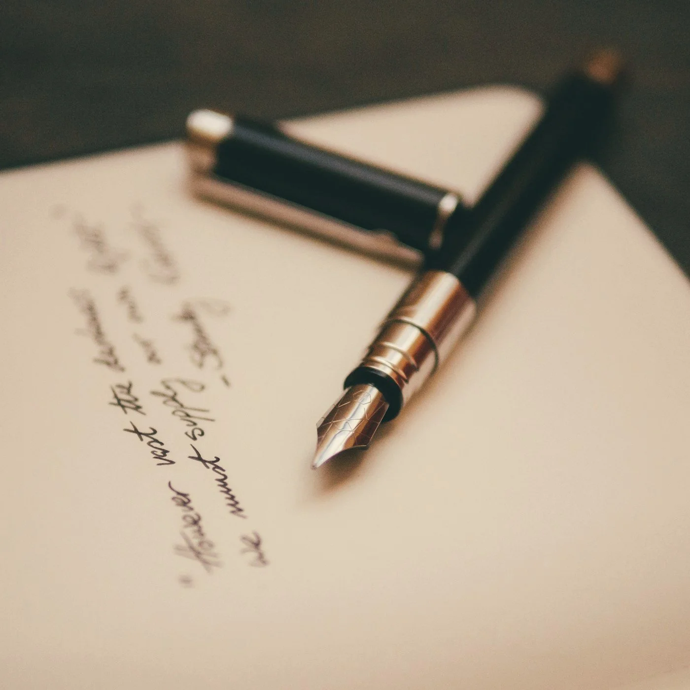 Gold and black fountain pen resting on handwritten paper beside a clipboard