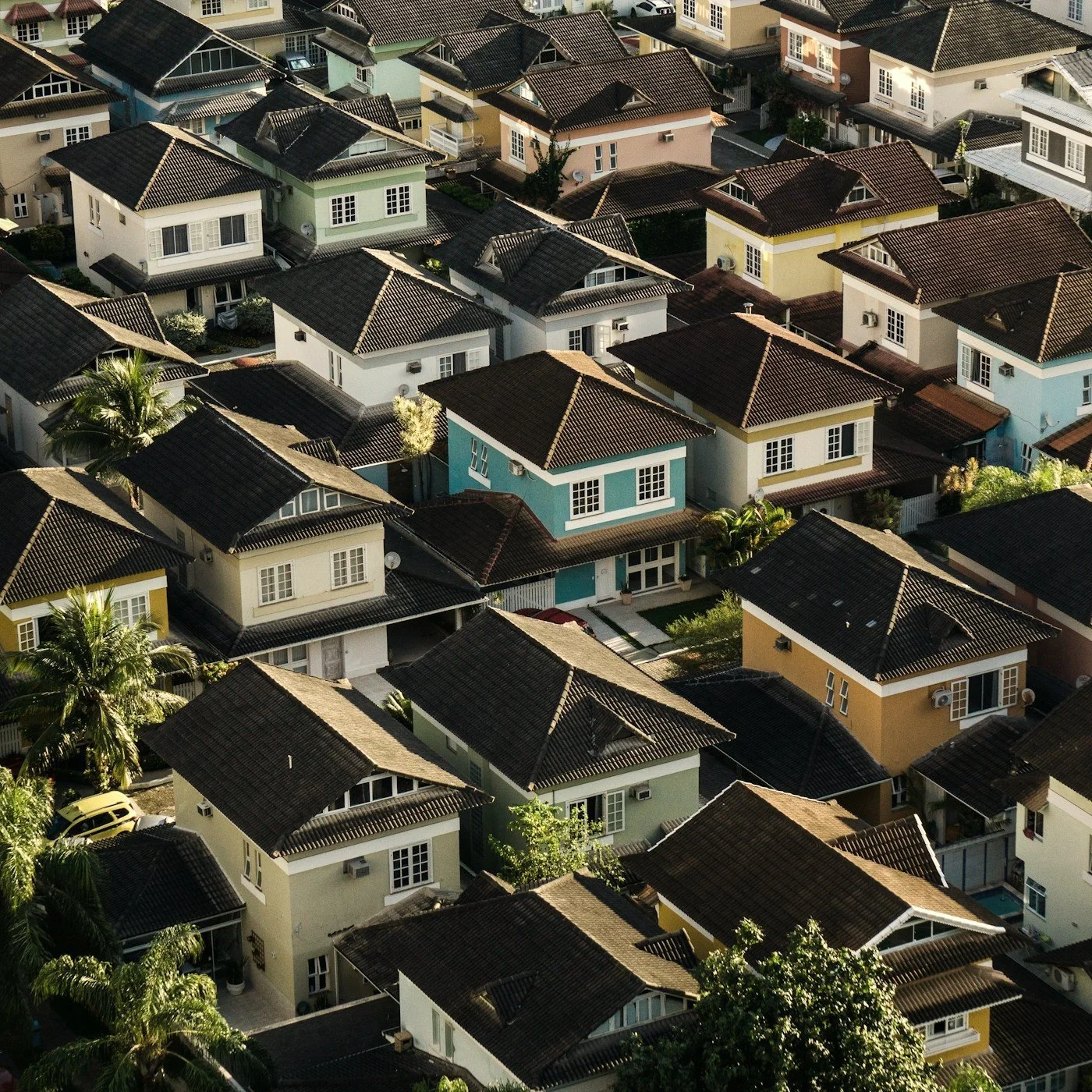Aerial view of a dense residential neighborhood with colorful houses, dark tiled roofs, palm trees, and narrow streets