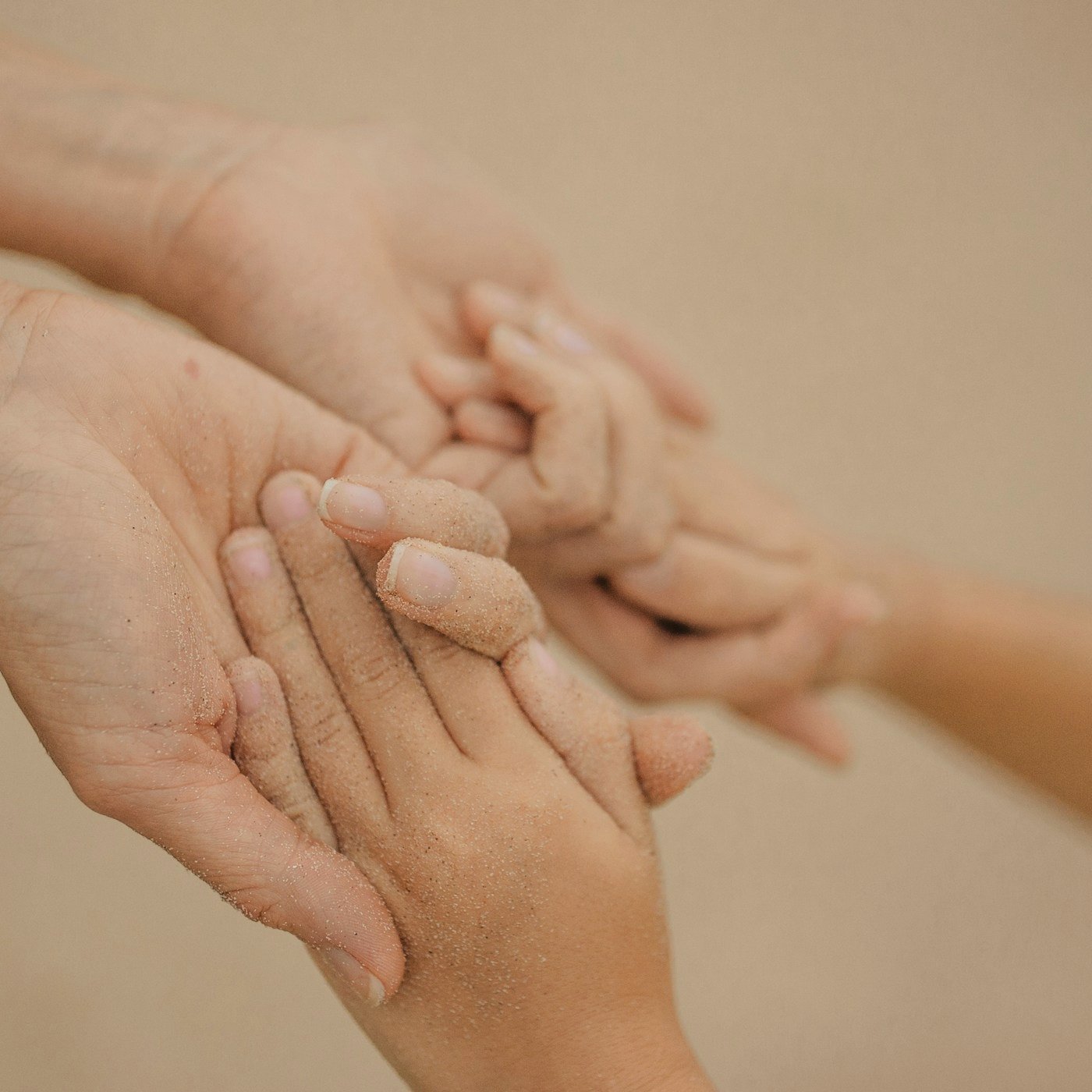 Close-up of a parent holding a sandy child's hand at the beach