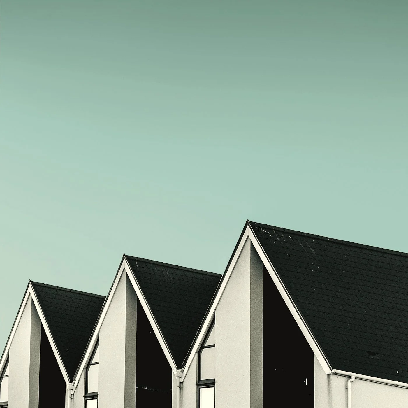 Row of modern white townhouses with steep black gabled roofs against a pale green sky
