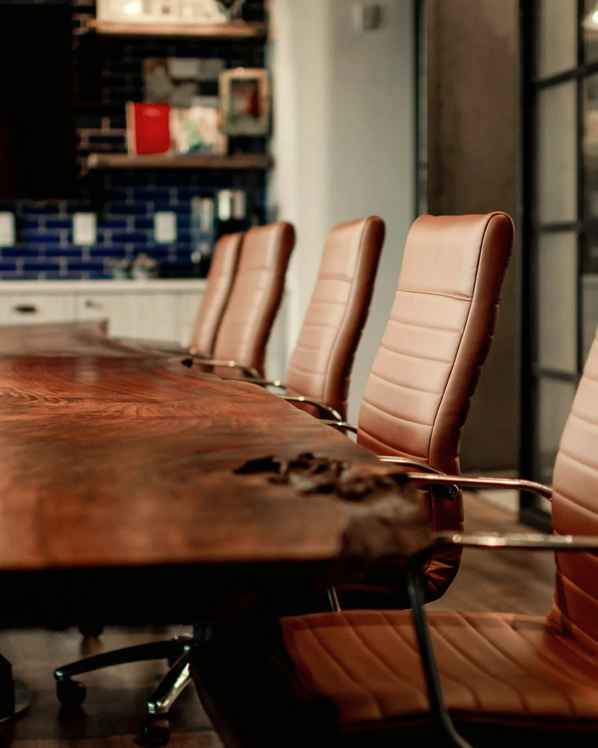 Brown leather office chairs around a large wooden conference table in a modern kitchen