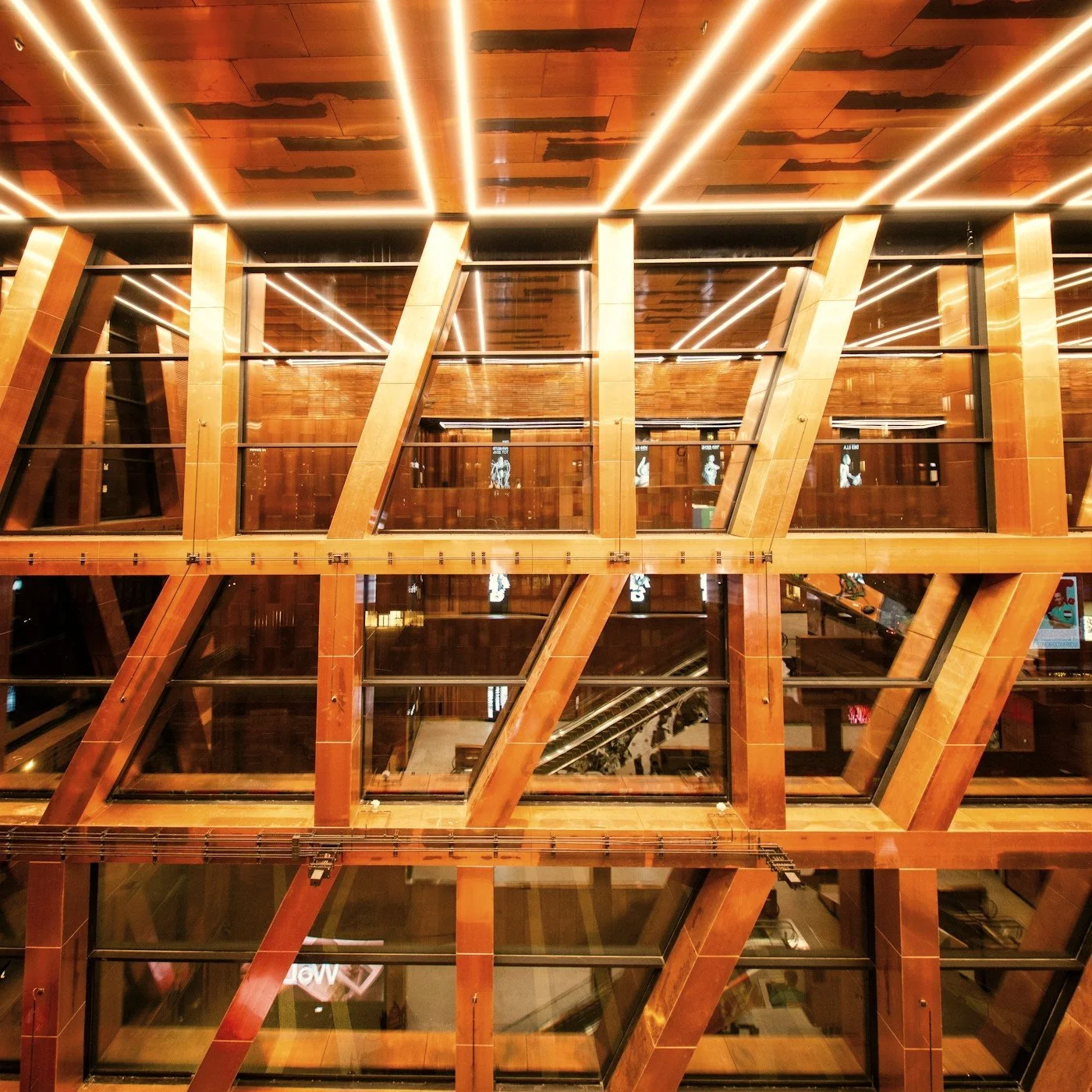 Modern atrium with geometric wooden beams, glass walls, escalators, and glowing linear ceiling lights.