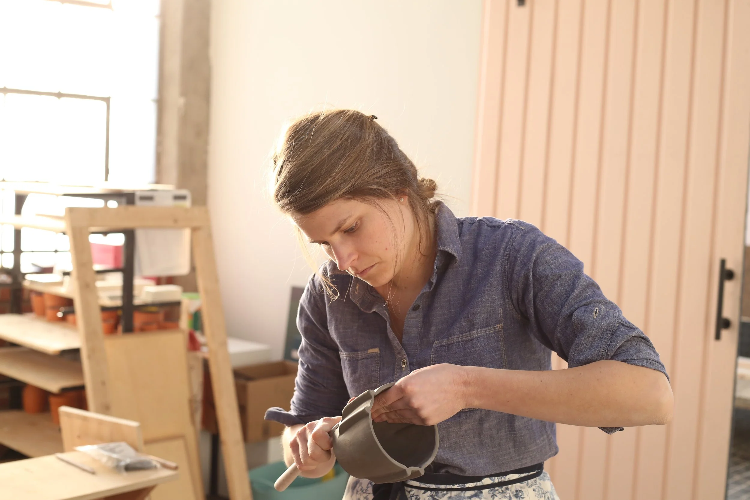 A woman working on a craft project, possibly painting or assembling an object, in a well-lit room.