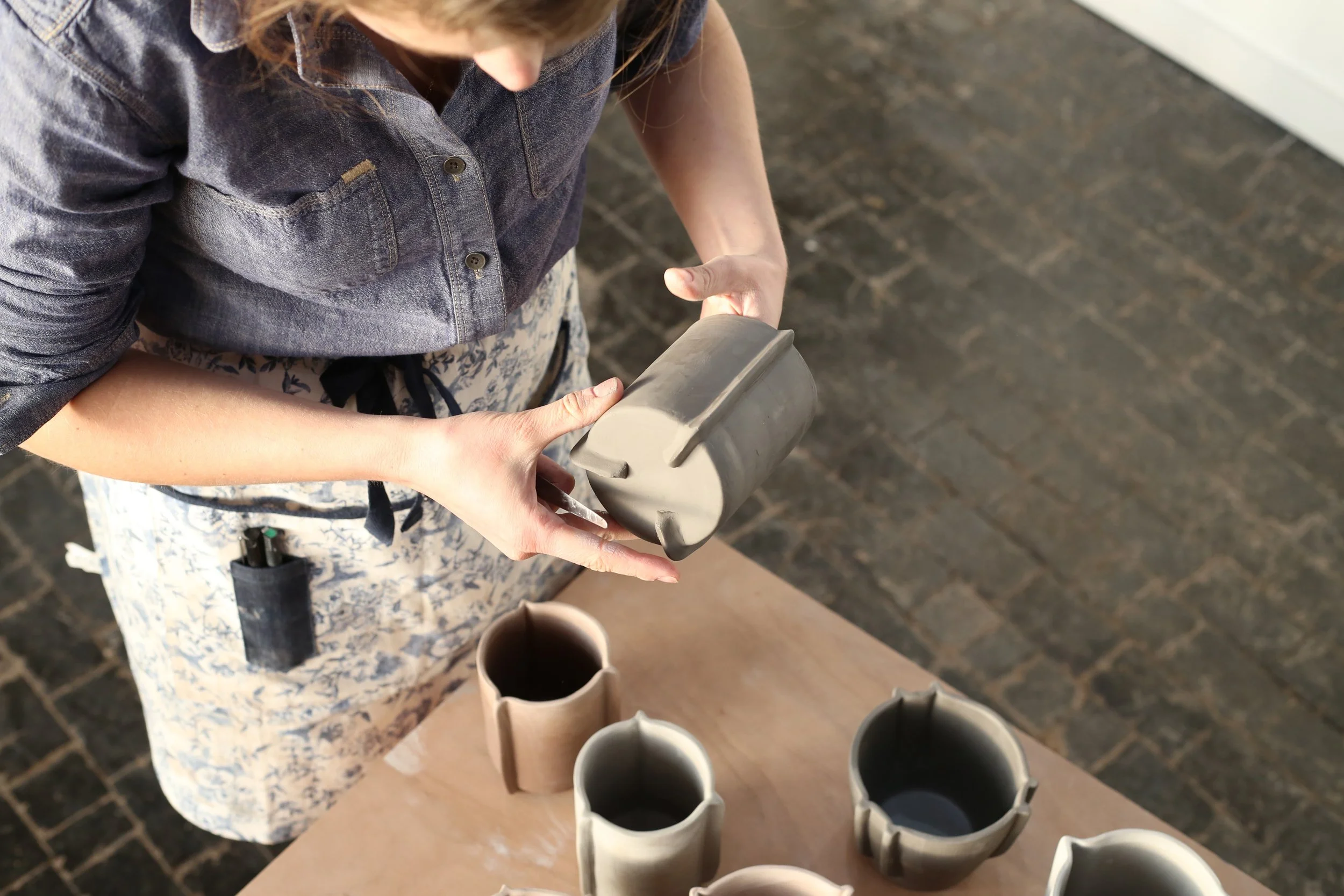 Person holding a gray icing piping tip over a countertop with several other piping tips and a cup of coffee.