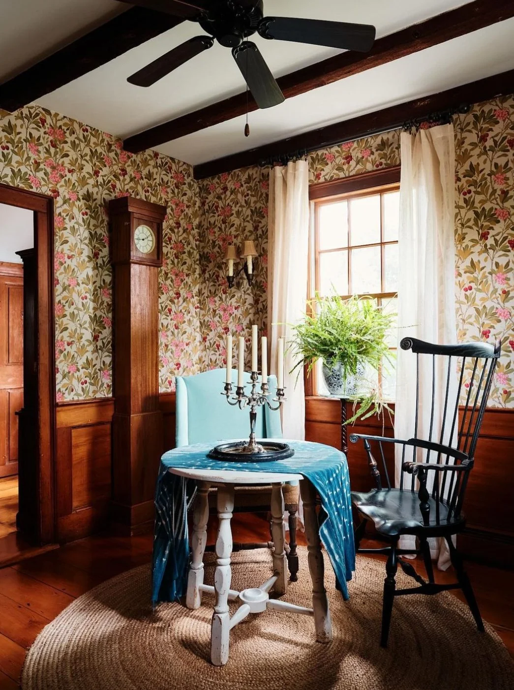 Historic dining nook with floral wallpaper, dark wood paneling, vintage chairs, and a blue upholstered accent chair